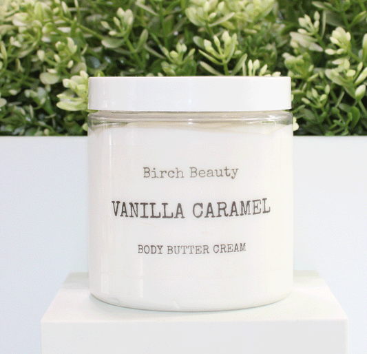 Jar of 'Vanilla Caramel' body butter cream with 'Birch Beauty' branding on a light surface with greenery in the background.