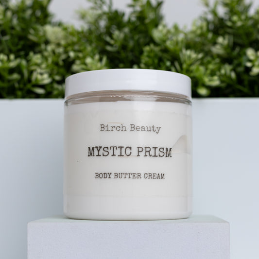 Jar of 'Mystic Prism' body butter cream with 'Birch Beauty' branding on a light surface with greenery in the background.