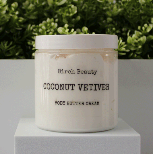Jar of 'Coconut Vetiver' body butter cream with 'Birch Beauty' branding on a light surface with greenery in the background. Handmade in Rhode Island. Made with limited ingredients.