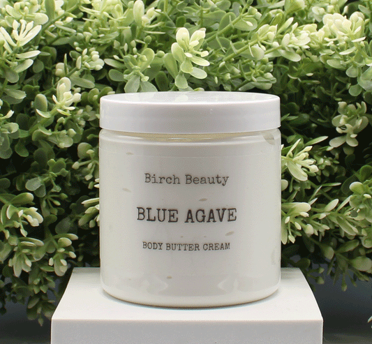 Jar of 'Blue Agave' body butter cream with 'Birch Beauty' branding on a light surface with greenery in the background. Handmade in Rhode Island. Made with limited ingredients.