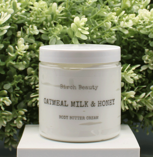 Jar of 'Oatmeal Milk & Honey' body butter cream with 'Birch Beauty' branding on a light surface with greenery in the background. Handmade in Rhode Island. Made with limited ingredients.