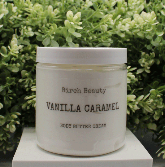 Jar of 'Vanilla Caramel' body butter cream with 'Birch Beauty' branding on a light surface with greenery in the background. Handmade in Rhode Island. Made with limited ingredients.