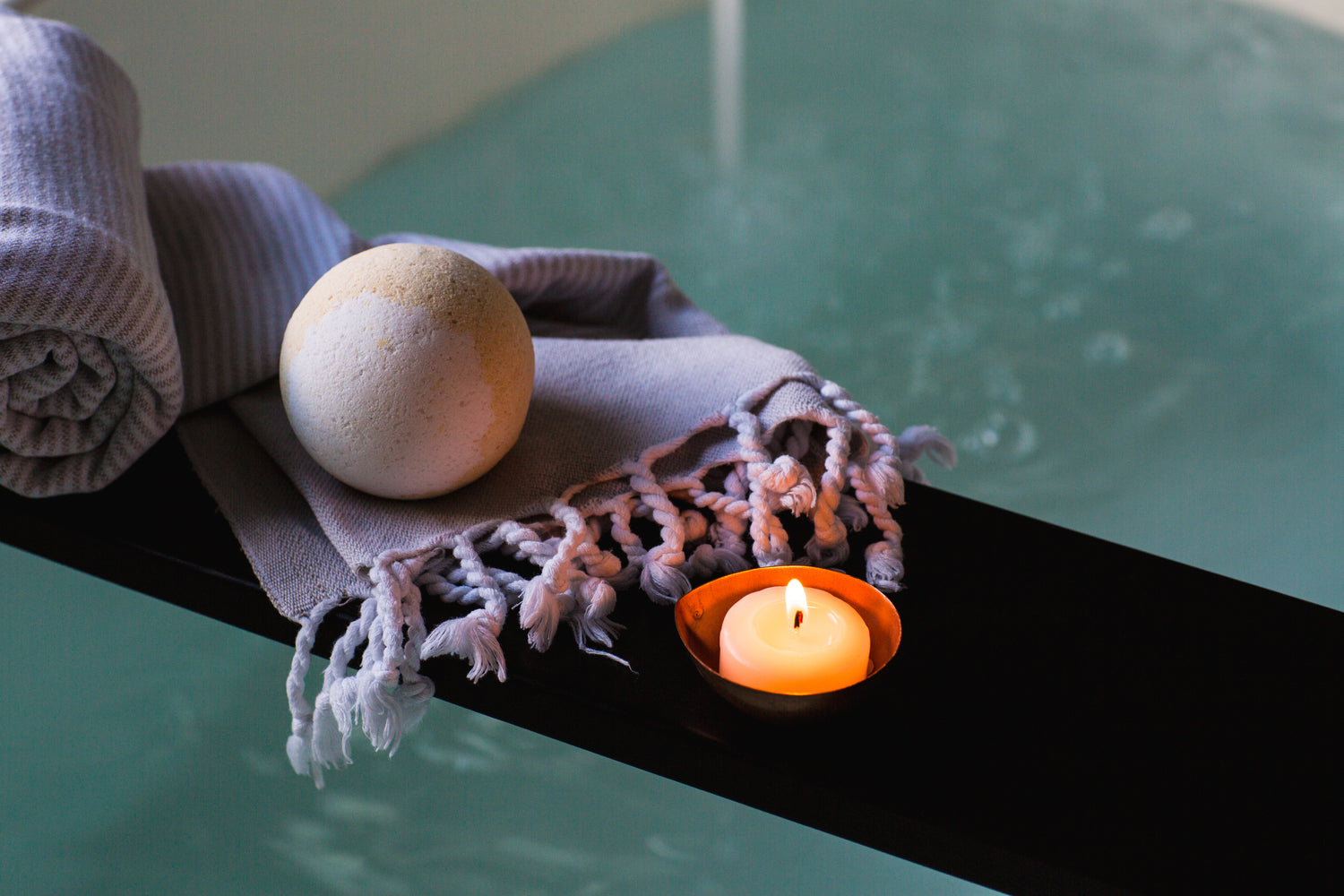 Bath bomb and candle resting on a bathtub plank